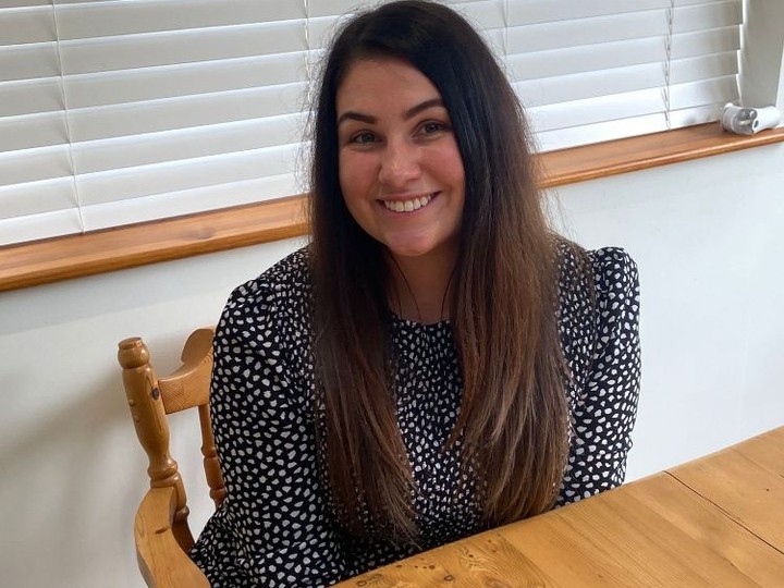 Image of female Coleg Cymraeg Cenedlaethol Branch Officer sitting at a wooden table. 